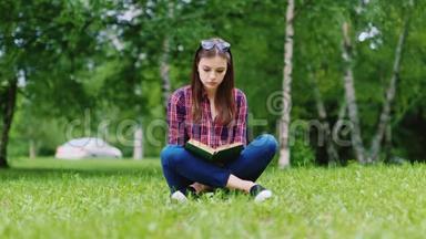 迷人的女学生在公园里看书，坐在草坪上